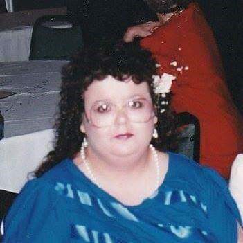 Woman with glasses in a blue dress with a flower in her hair sitting at a table